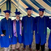Five graduates pose together under outdoor tent